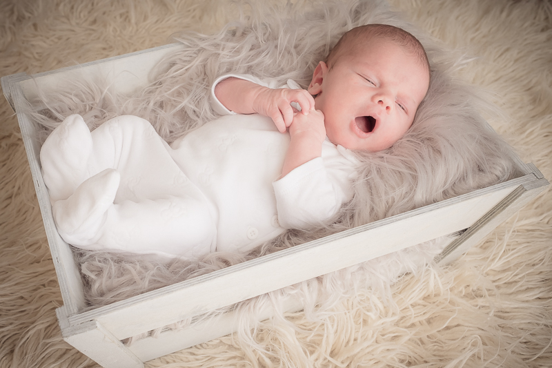 Yawning newborn in a white crate
