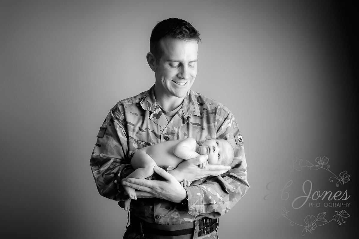 newborn baby held in soldier father's arms