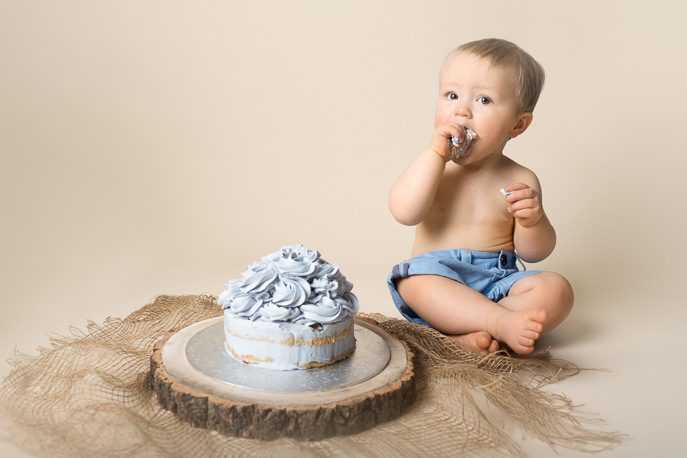 baby boy in blue shorts with blue cake at photoshoot