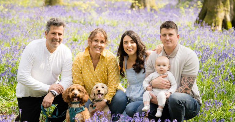 Young couple with baby posing in the bluebell woods Hampshire with grandparents and their dogs.