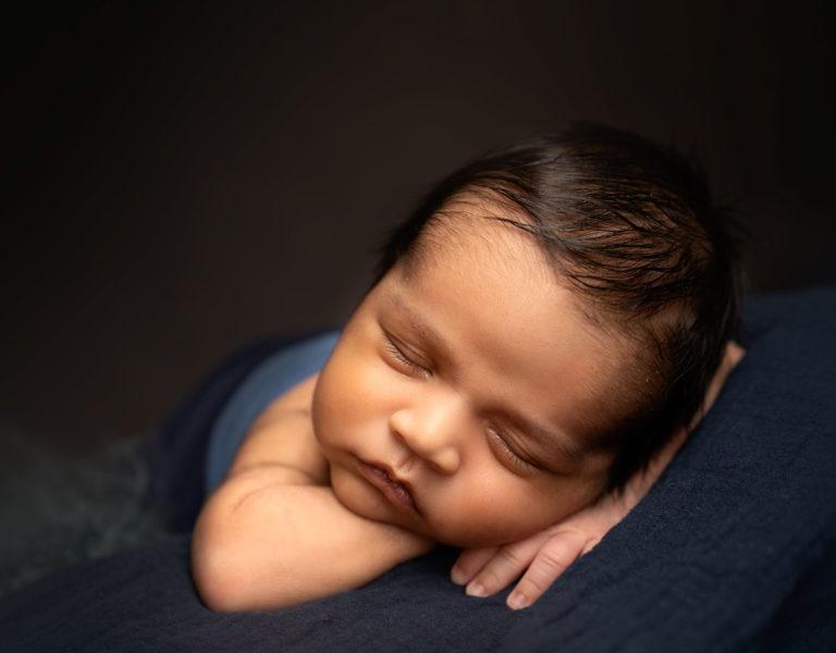 Close up of newborn baby sleeping with head on his hands, lying on a blue blanket, taken by newborn photographer near Basingstoke.