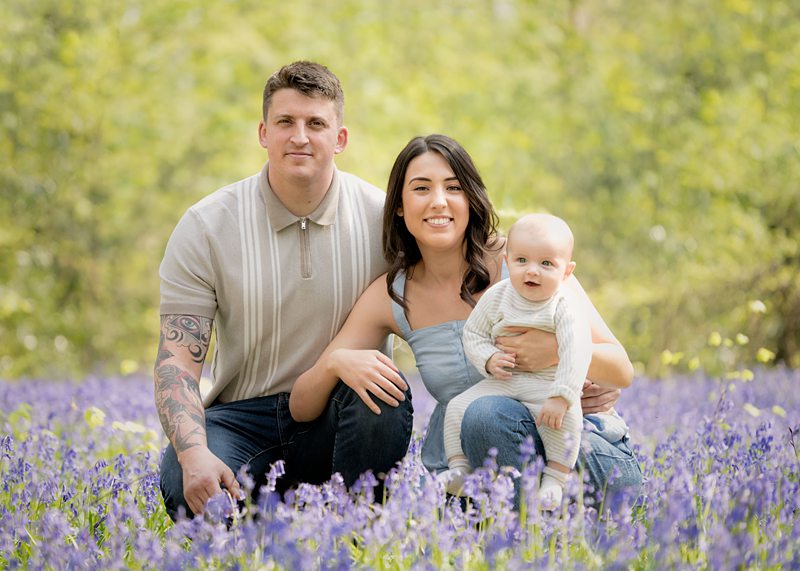 Young family crouching amidst the flowers in the bluebell woods.