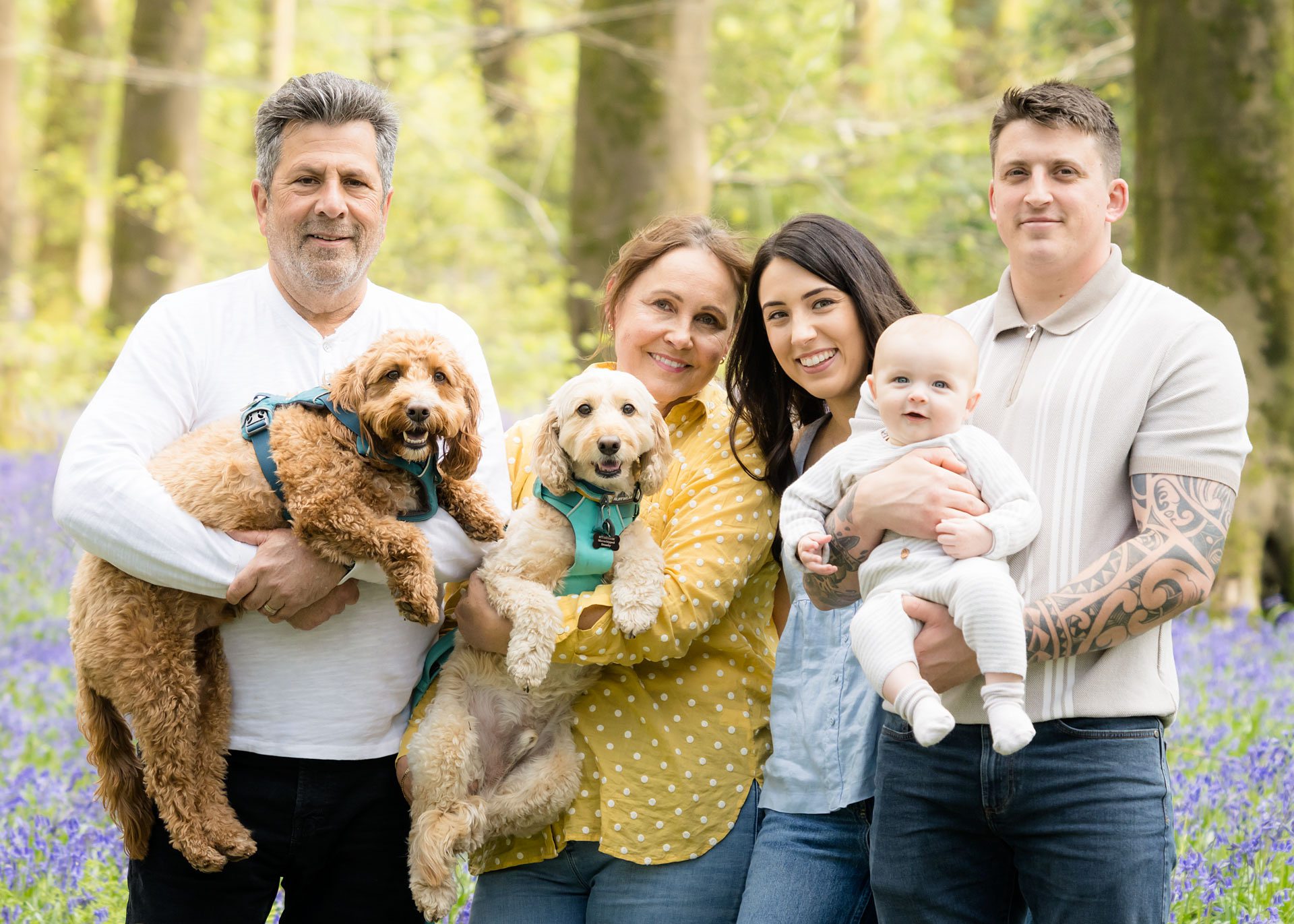 Young couple with baby, grandparents and dogs, smiling in the bluebell woods.