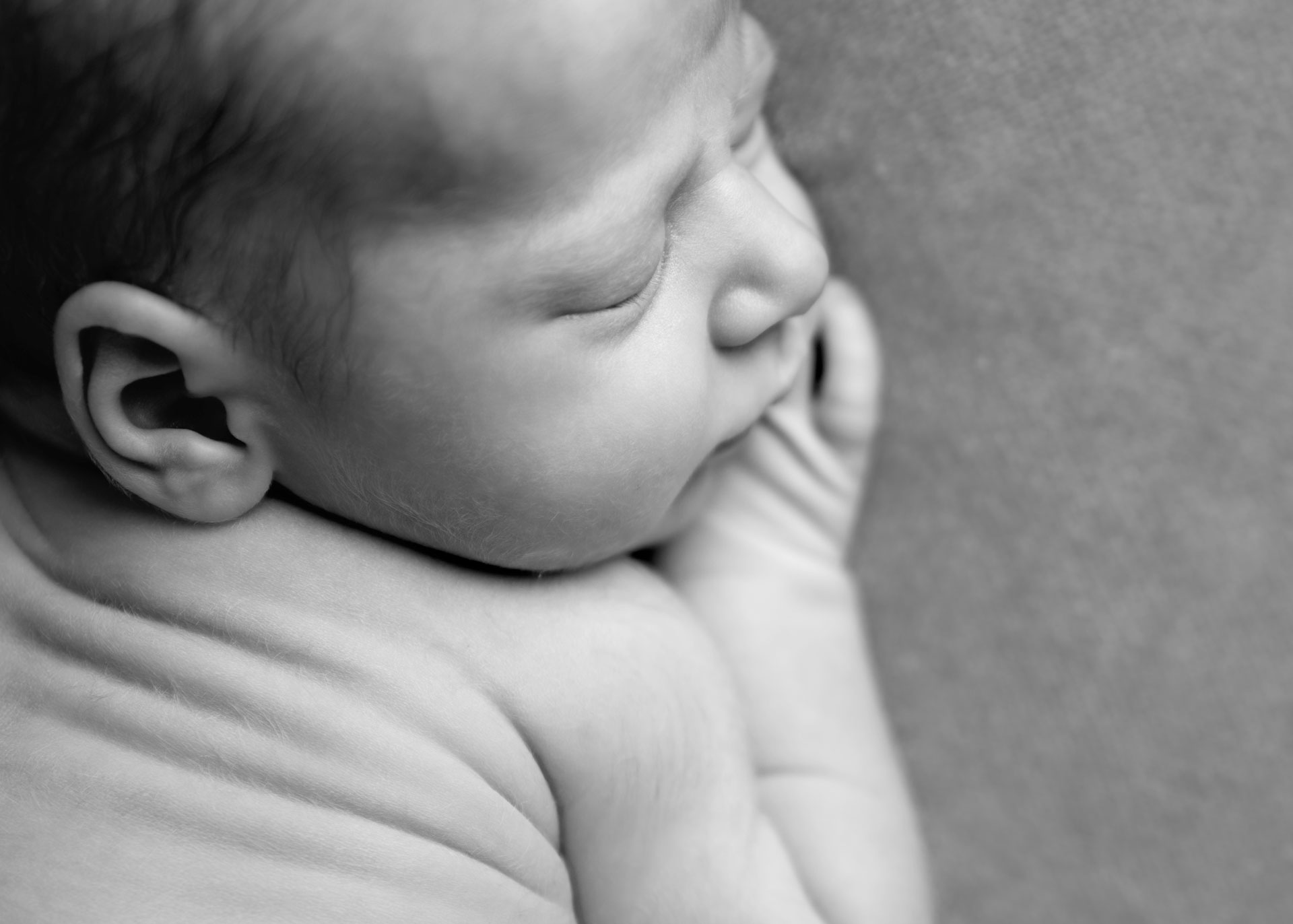 Black and white close up of a newborn baby's head and shoulders, showing fine downy hair, taken by a Hampshire newborn photographer.