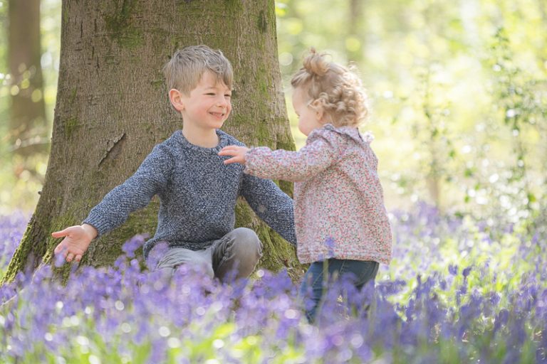 Brother and sister embracing beneath a tree in the bluebell woods.