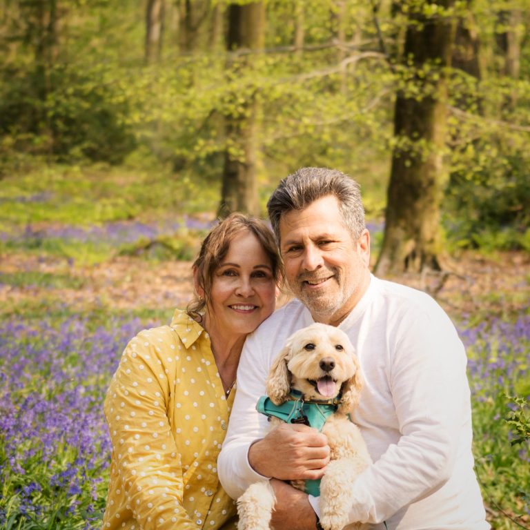 Couple posing smiling in the bluebell woods with their dog.