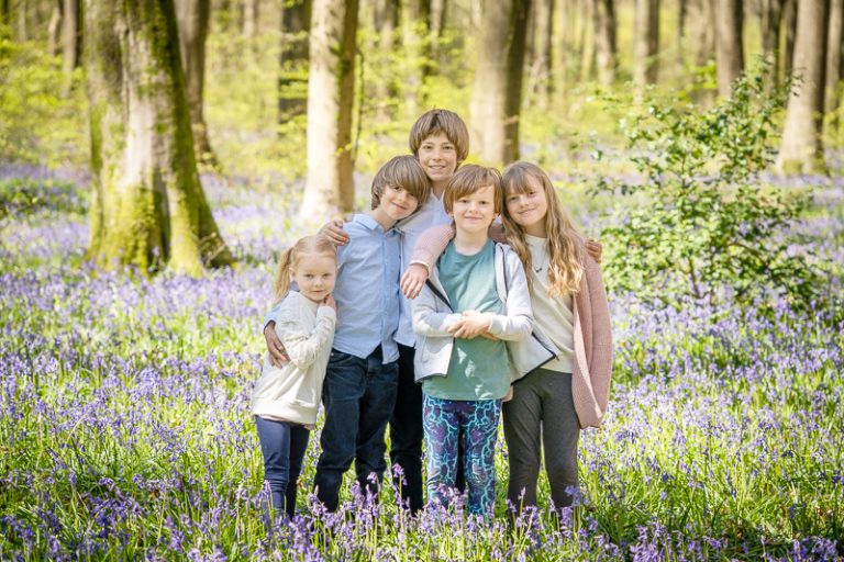 Five children posing in a group portrait in the sun dappled bluebell woods.
