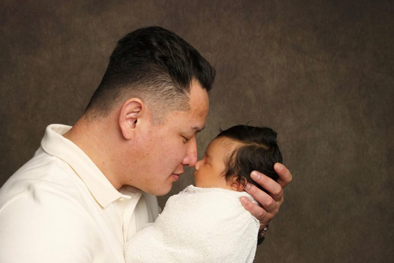 Father holding newborn baby, swaddled in white blanket, touching noses.