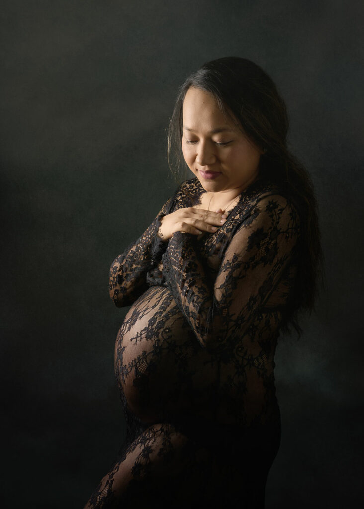 A radiant woman embracing her pregnancy, wearing a sheer lace dress, posing gracefully for a captivating maternity photoshoot.