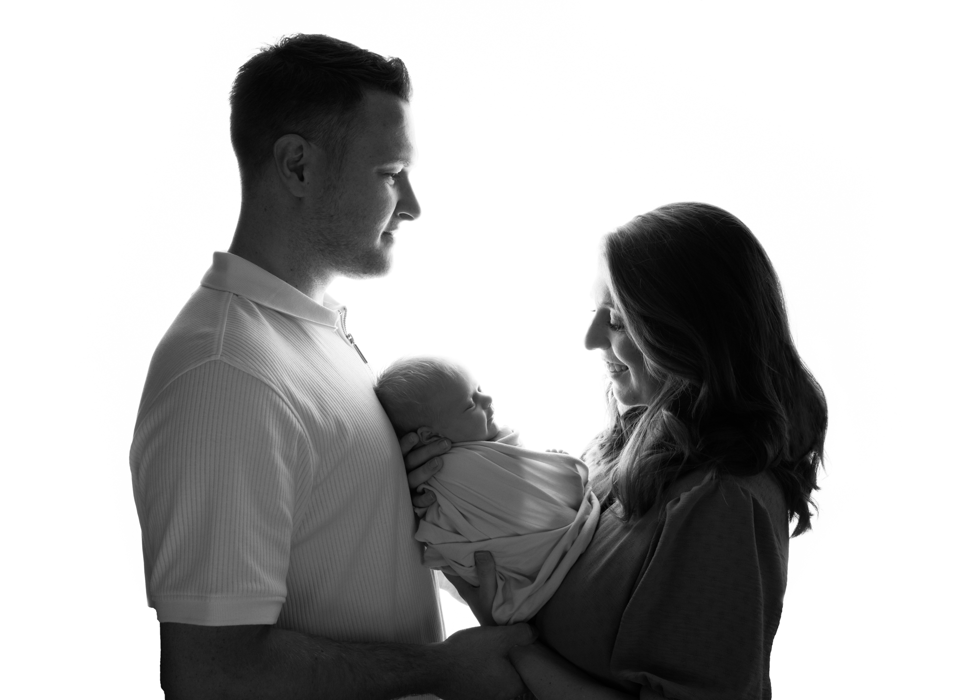 Couple posing with newborn baby in backlit shot at H Jones Photography studio in Hampshire.
