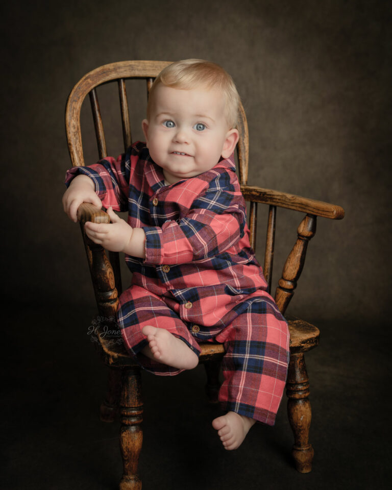 Portrait of young boy wearing Christmas pyjamas, sitting in a vintage child's chair, at H Jones photography studio in Hampshire.