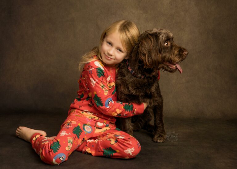 Portrait of young girl with long blonde hair, wearing Christmas pyjamas, cuddling her pet dog.