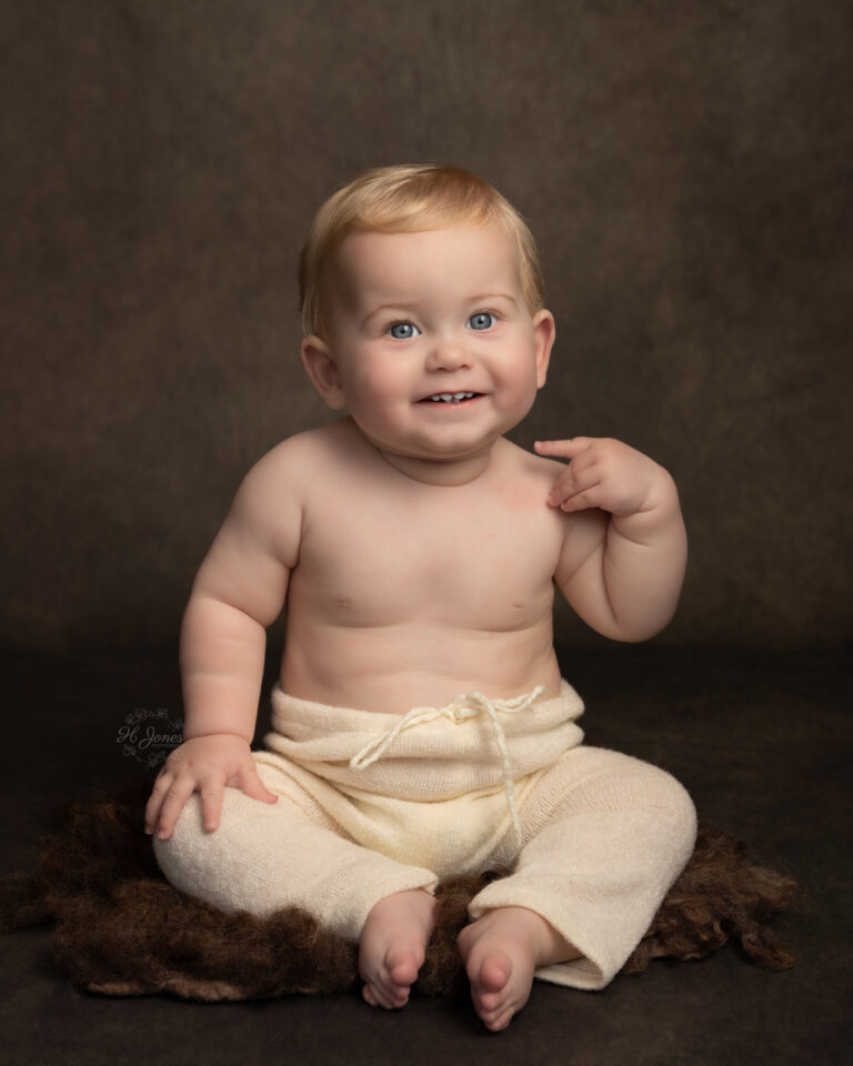 Portrait of small boy, wearing white knitted leggings, sitting on brown fur rug.