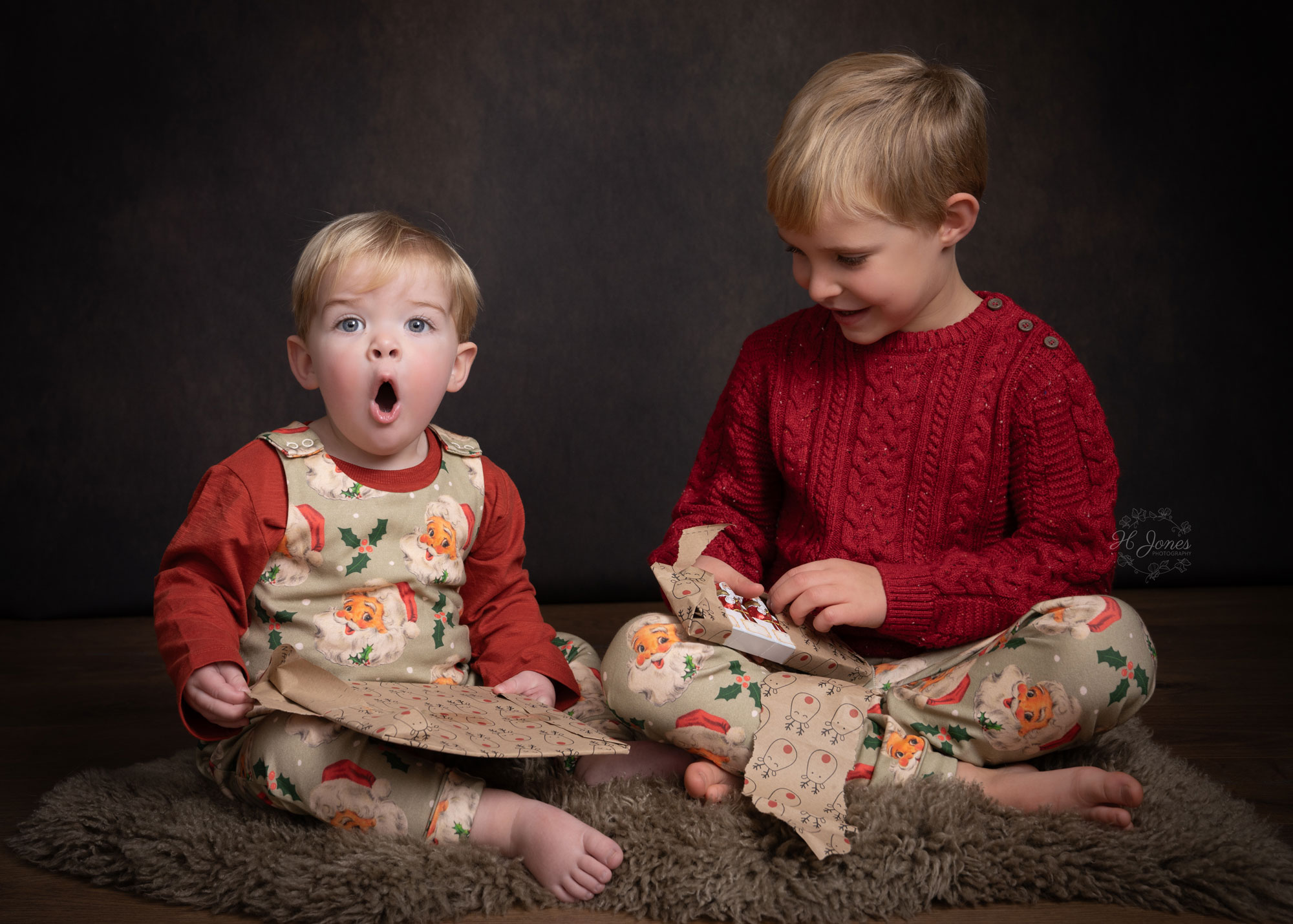 Two young brothers, sitting on a fur rug, excitedly opening presents during a Christmas photoshoot near Newbury.