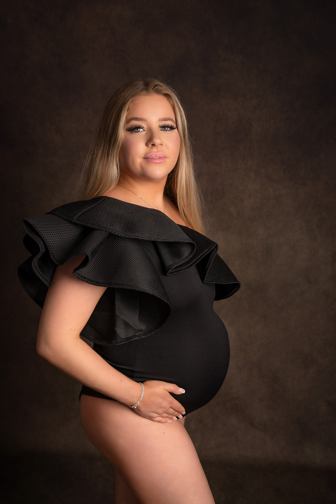 Pregnant lady wearing a black bodysuit with exaggerated shoulder detail, gazing at the camera.