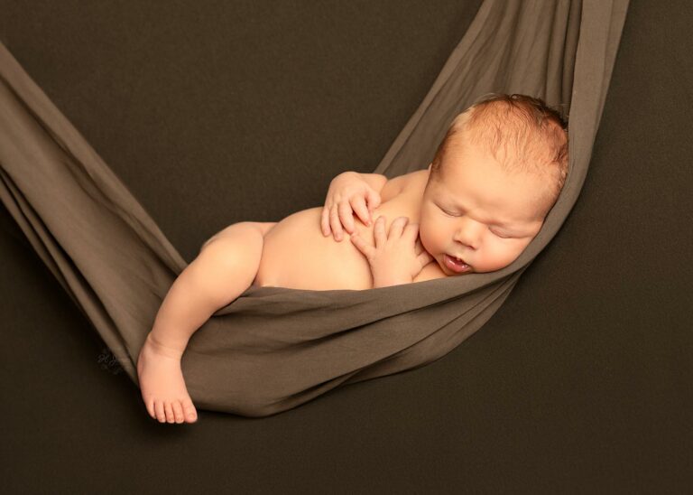 Newborn baby sleeping in a hammock, posed safely on a beanbag, at a photoshoot