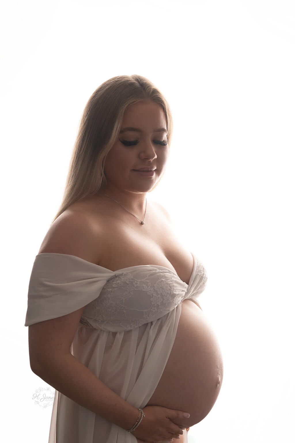 Pregnant lady wearing white maternity gown with bump exposed posing for a maternity photoshoot.