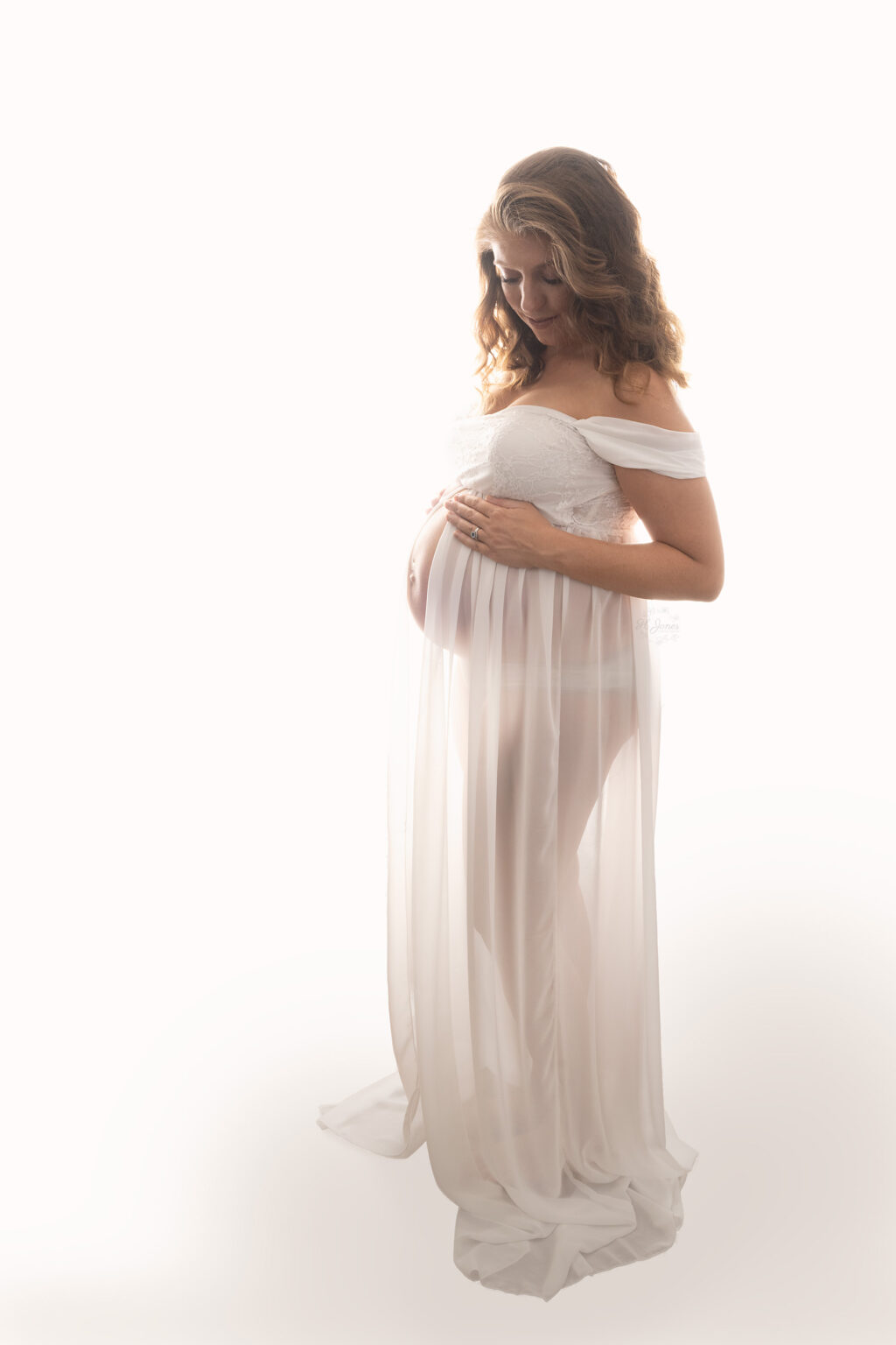 Full length backlit shot of pregnant lady in long white maternity gown.