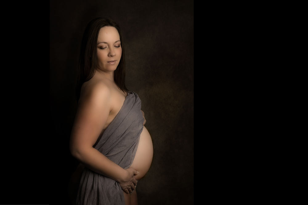 Pregnant woman posing in a photography studio in Andover, with bump exposed, wearing a grey silk fabric.