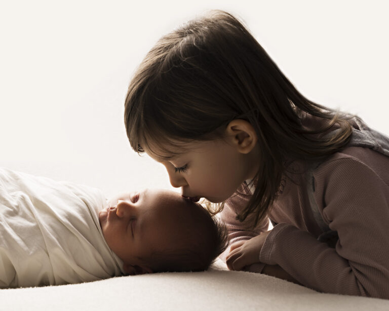 Two year old girl kissing the forehead of her baby brother.