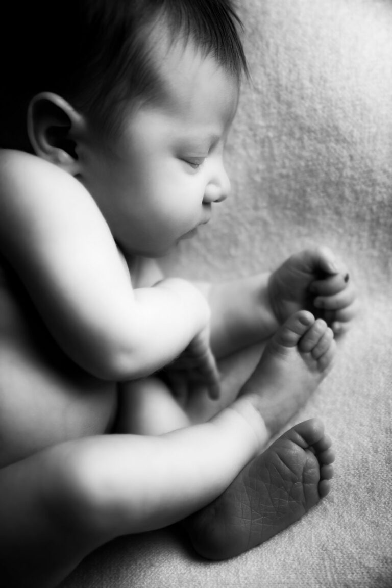 Black and white image of a newborn baby sleeping on their side.