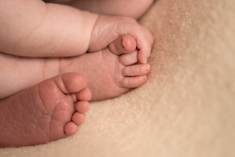 Close up image of a newborn baby's hand holding their feet, as they lie curled up on a blanket.