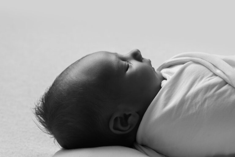 Black and white image of a newborn baby sleeping got their back, shown from the side.