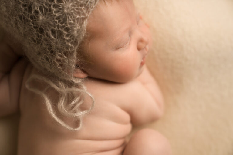 Close up of a newborn baby showing the folds in the skin on their back, as they are curled up on their front, sleeping.