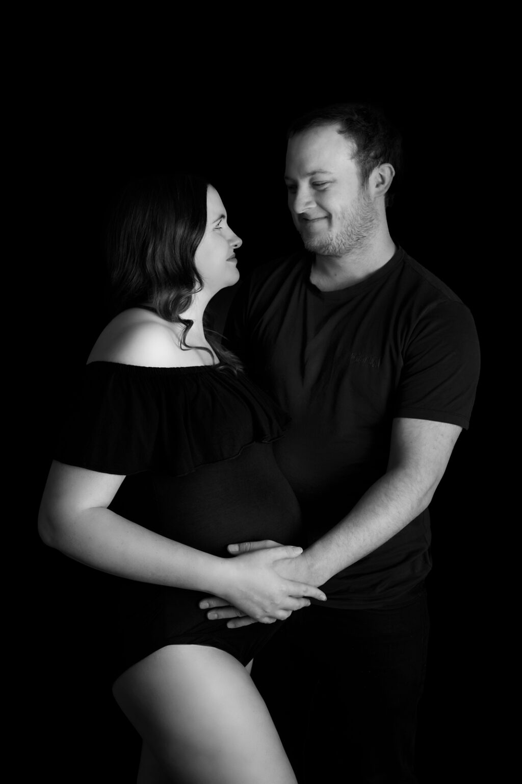 Expecting couple posing in black and white, smiling into each others eyes.