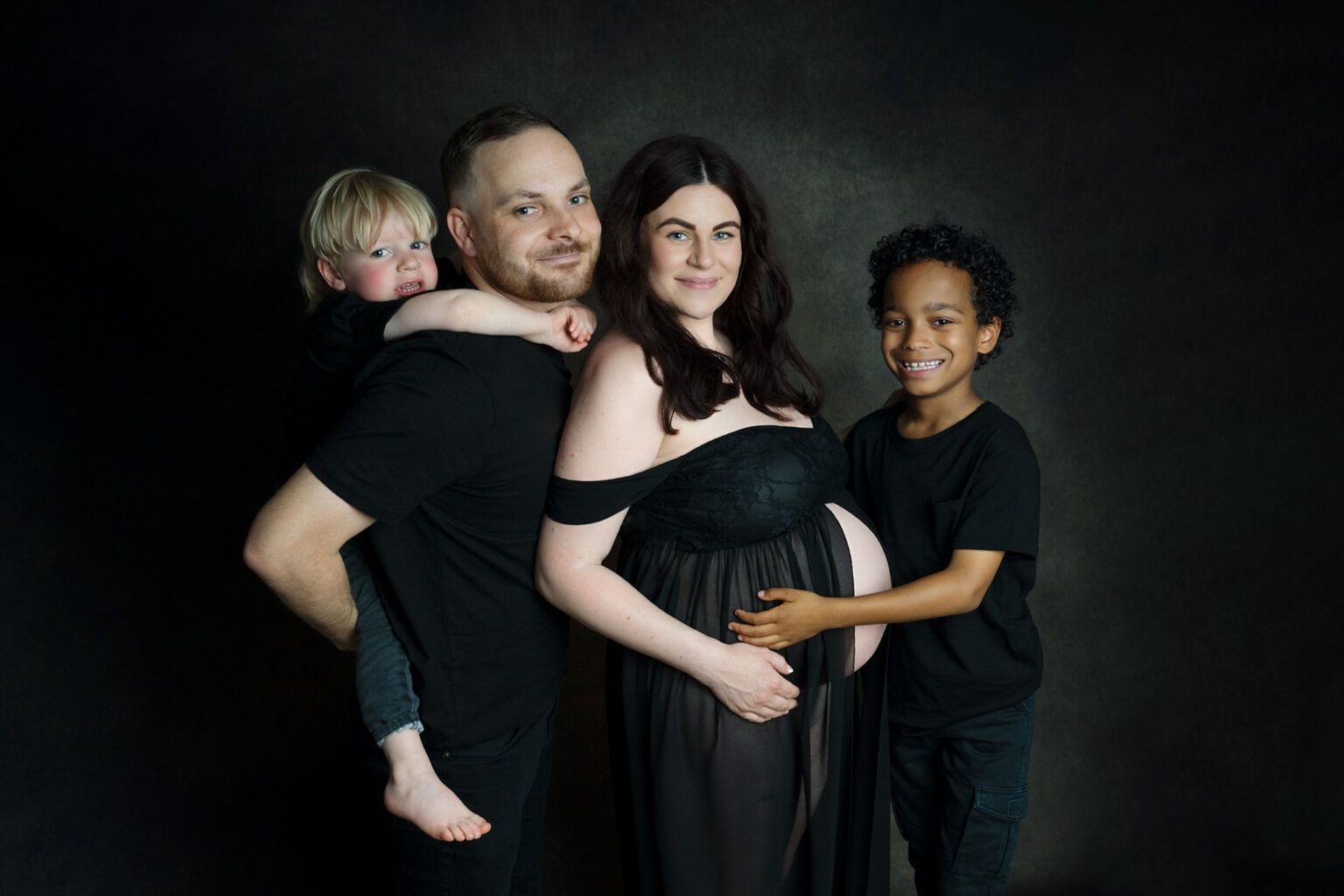 Smiling family of four with pregnant mum, all dressed in black, at a Hampshire maternity photoshoot