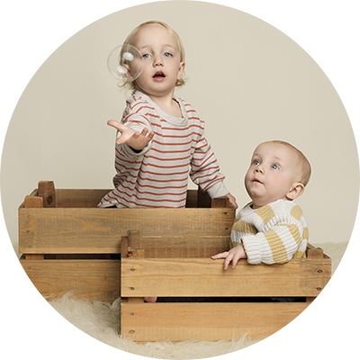 Circular image showing two young brothers dressed in striped t-shirts, playing with bubbles, sitting in wooden crates.