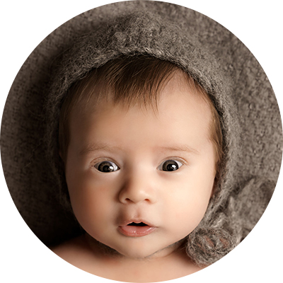 Close up of the face of a baby boy, wearing a grey knitted hat, laying on a matching grey blanket.