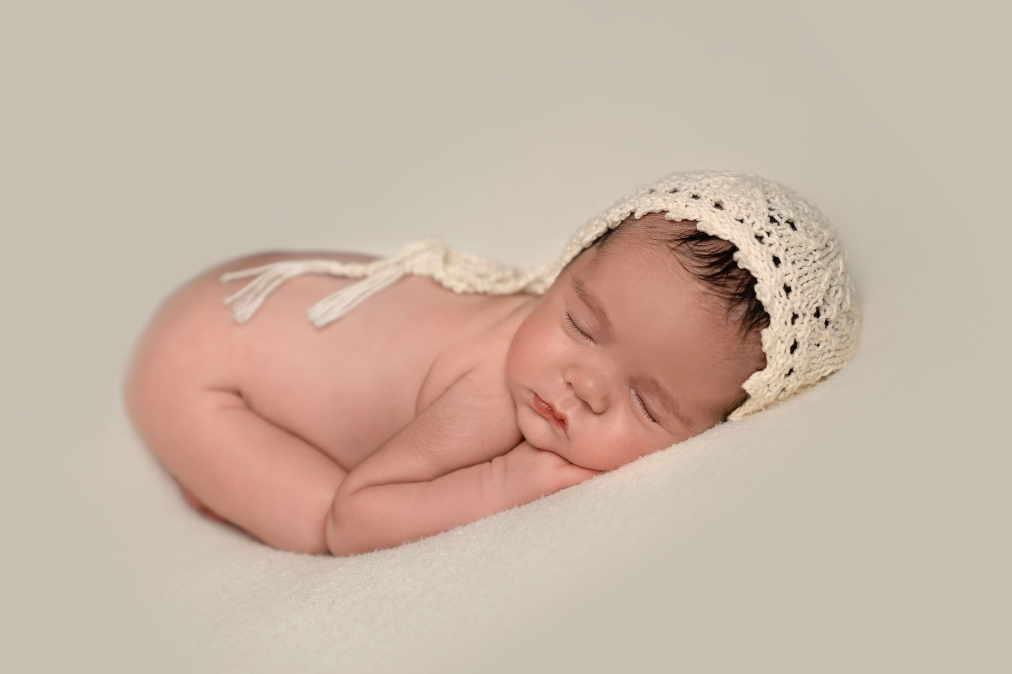 Newborn baby girl curled up on a cream coloured blanket, at a newborn photoshoot near Salisbury