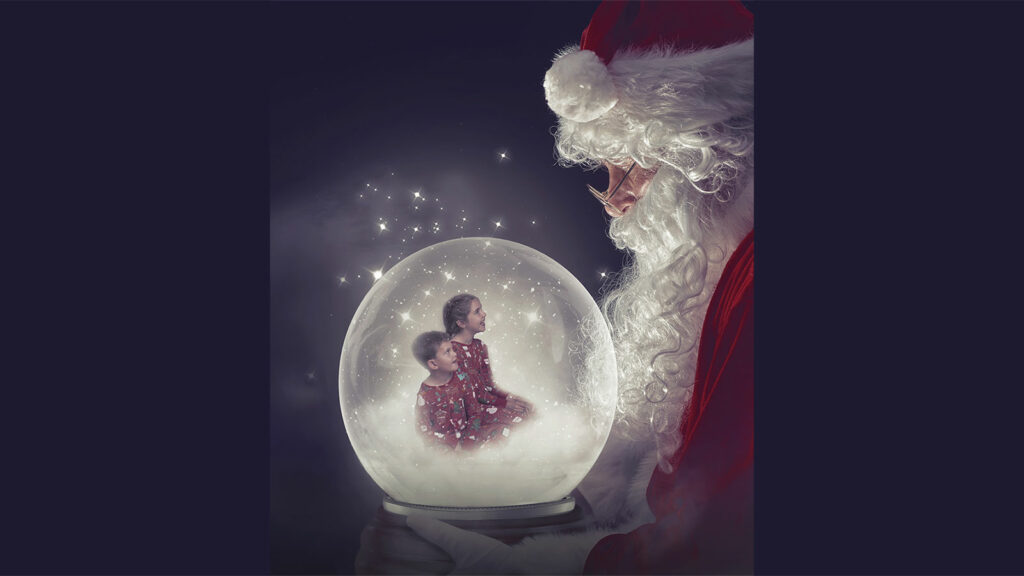 Brother and sister in Christmas pyjamas sitting inside a snow globe held by Santa at a Christmas Photoshoot in Hampshire