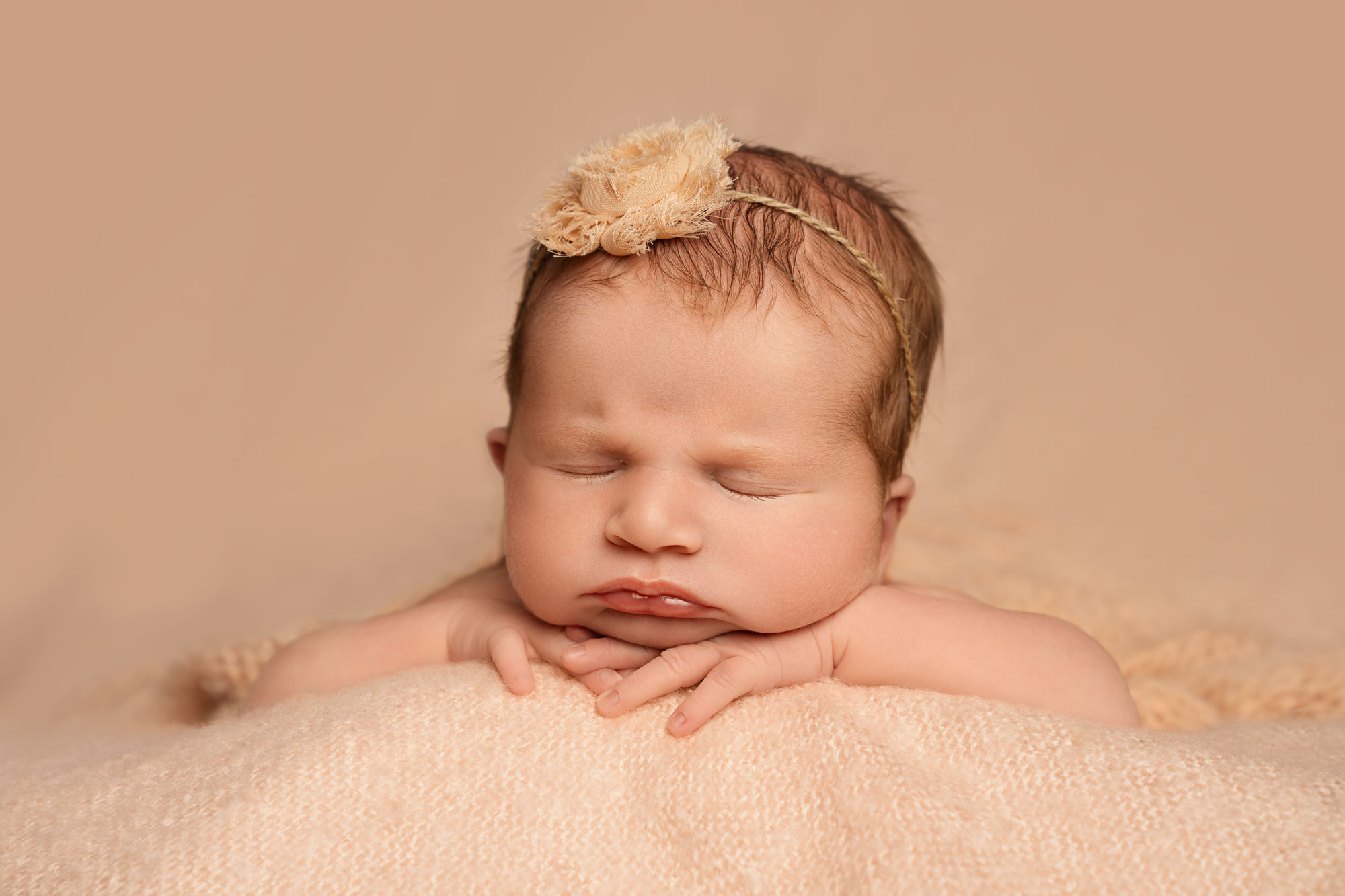 Newborn baby girl with flower in her hair, head on her hands.