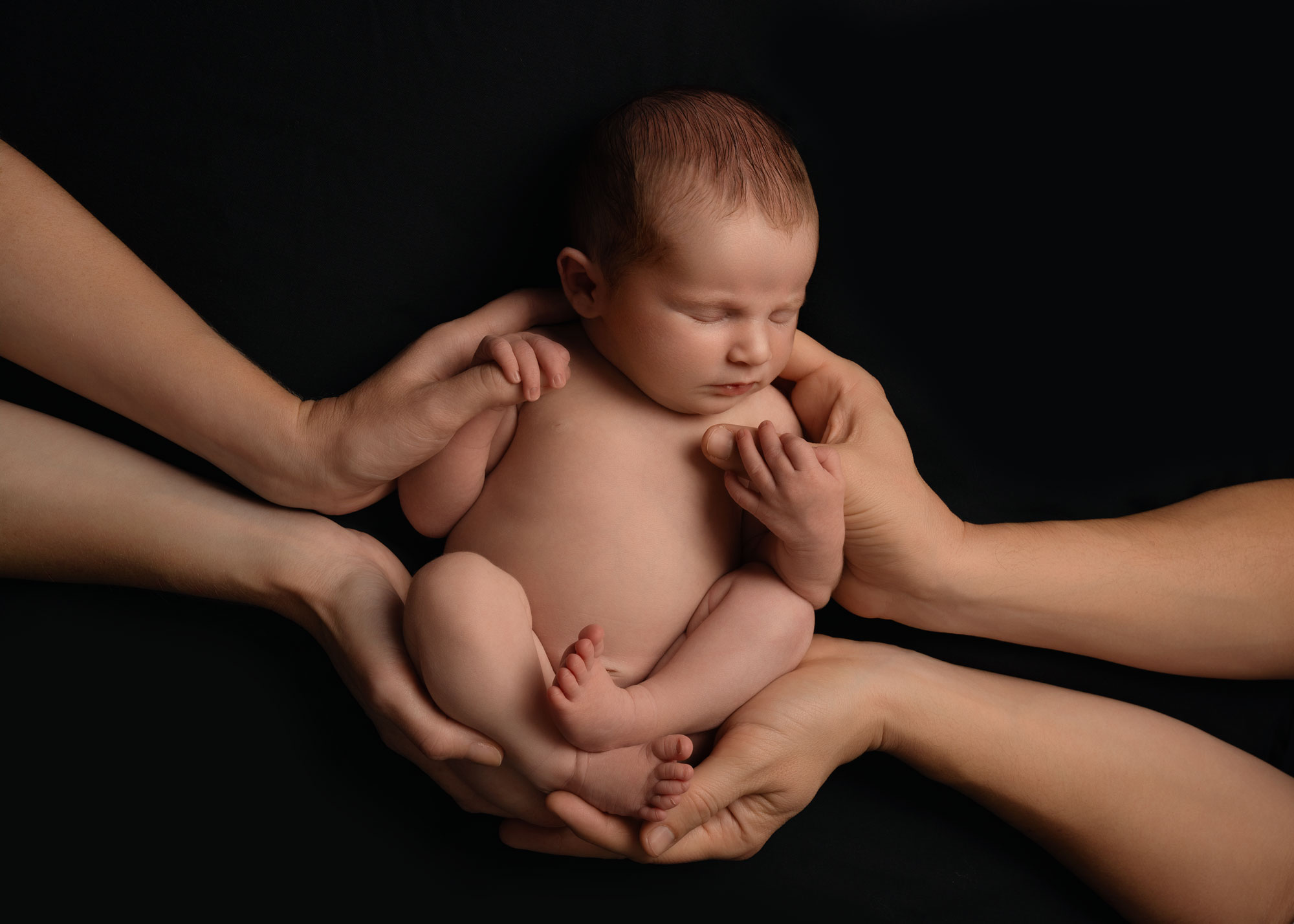 Newborn baby held in parents hands, set against a black backdrop, at a newborn photoshoot near Southampton