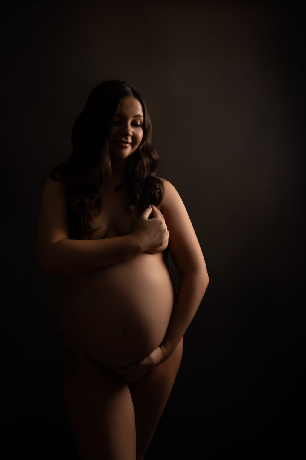 A nude pregnant woman cradles her bump, in a maternity photoshoot by H Jones Photography in Andover, Hampshire.