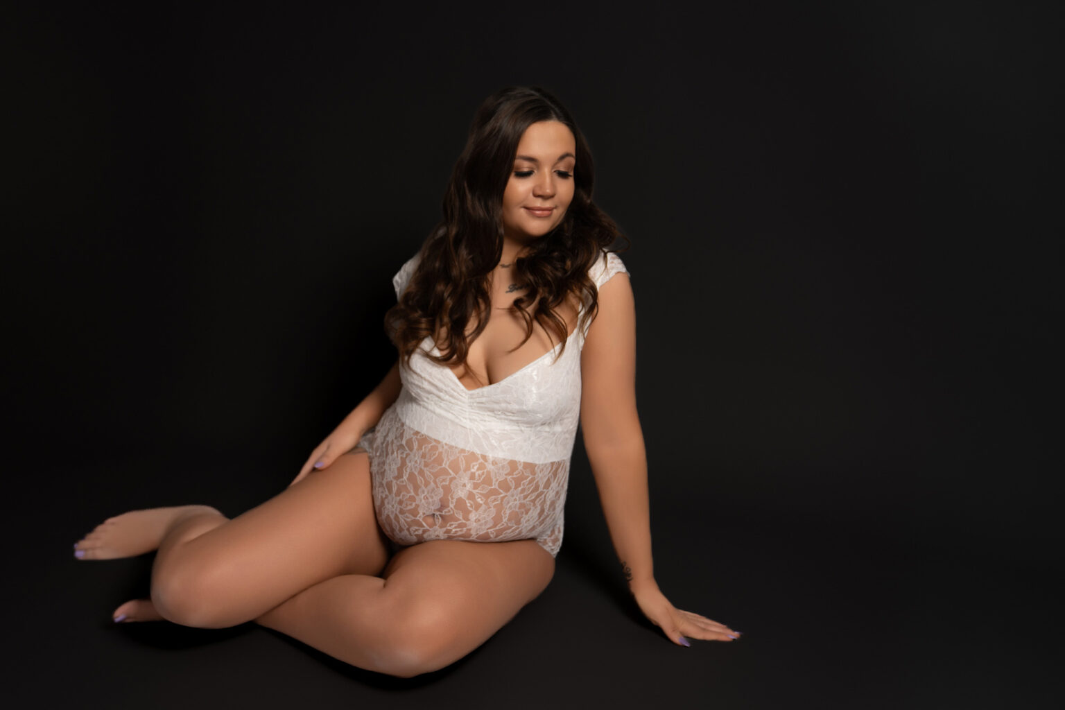 A pregnant woman sits on the floor of a photography studio in Andover Hampshire for a maternity photoshoot.