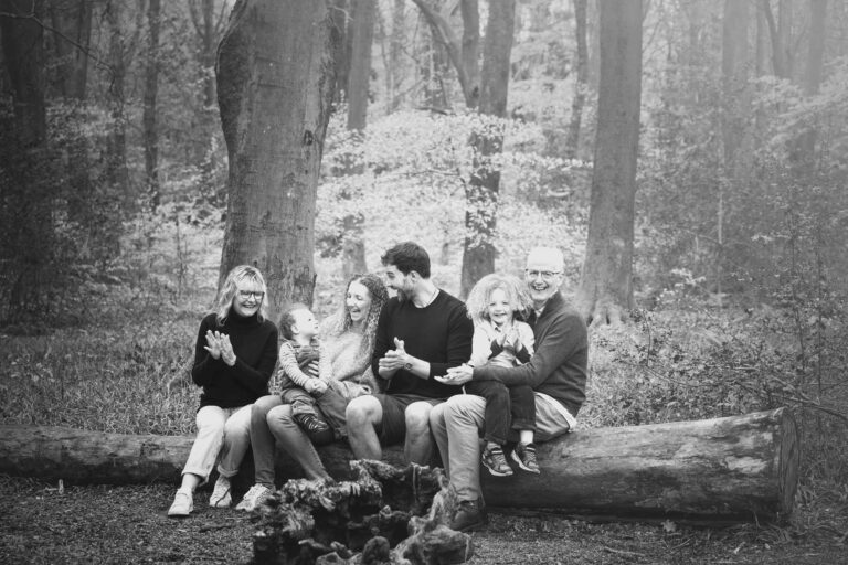 Black and white image of a family sitting on a fallen tree in the bluebell woods in hampshire