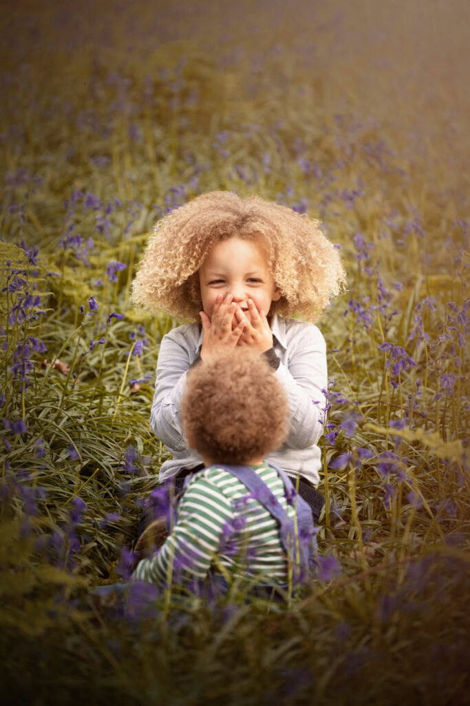 Two young brothers sitting and laughing in a natural outdoor family photoshoot at a bluebell wood, by H Jones Photography.