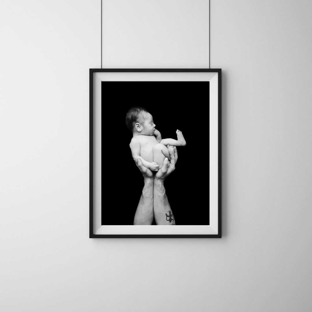 Hanging framed print of a newborn baby held in father's hands