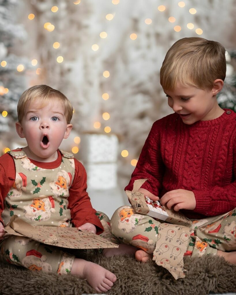 Brothers in festive outfits unwrapping Christmas presents during a studio photoshoot with twinkling lights in Hampshire.
