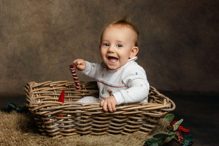 One year old boy in Christmas pyjamas, sitting in a small basket at a Hampshire photoshoot.