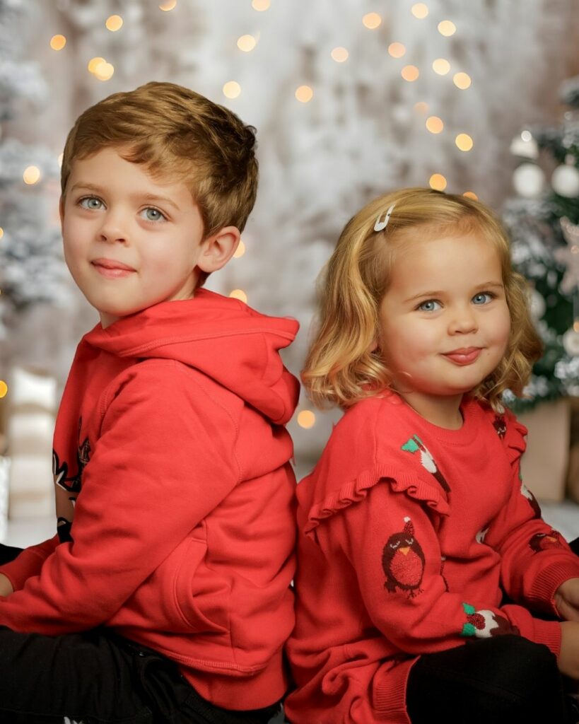 Smiling brother and sister in matching red Christmas jumpers posing together for a festive family photoshoot in Hampshire.