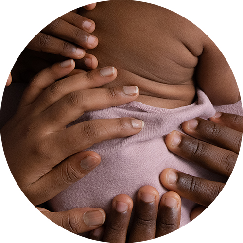 Close-up photograph of a newborn baby wrapped in a soft lavender blanket, surrounded by the gentle hands of family members holding and supporting the baby; warm, intimate newborn portrait by a Hampshire photographer.