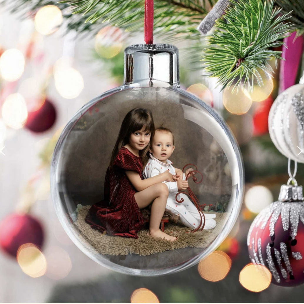Christmas bauble hanging on a tree, with a photo of children by H Jones Photography inside.