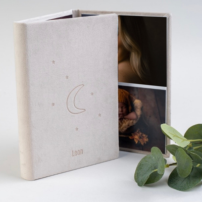 Light grey suede winged folio with a moon and stars embossed on the cover, personalised with the name Leon, displayed open to show professional newborn and family photographs.