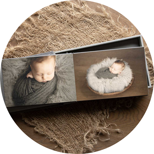 Luxury newborn photo album opened to show two soft, neutral-toned baby portraits, beautifully presented on a textured fabric background, created by a professional newborn photographer in Hampshire.