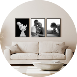 Set of three black and white framed newborn and family portraits displayed as wall art above a sofa in a bright, neutral living room, showcasing timeless baby photography by a Hampshire newborn photographer.
