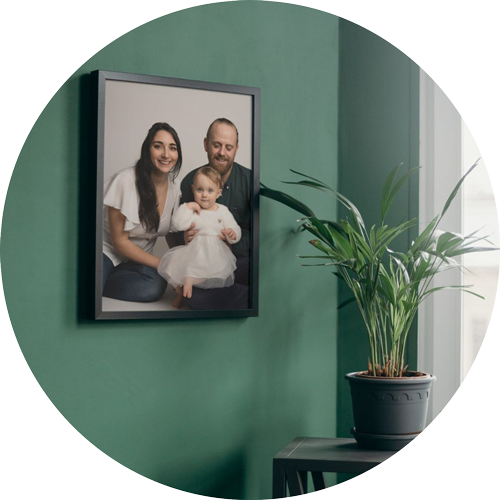 Framed family portrait of parents and their baby displayed as wall art on a green feature wall, styled in a modern home interior and photographed by a professional family photographer in Hampshire.